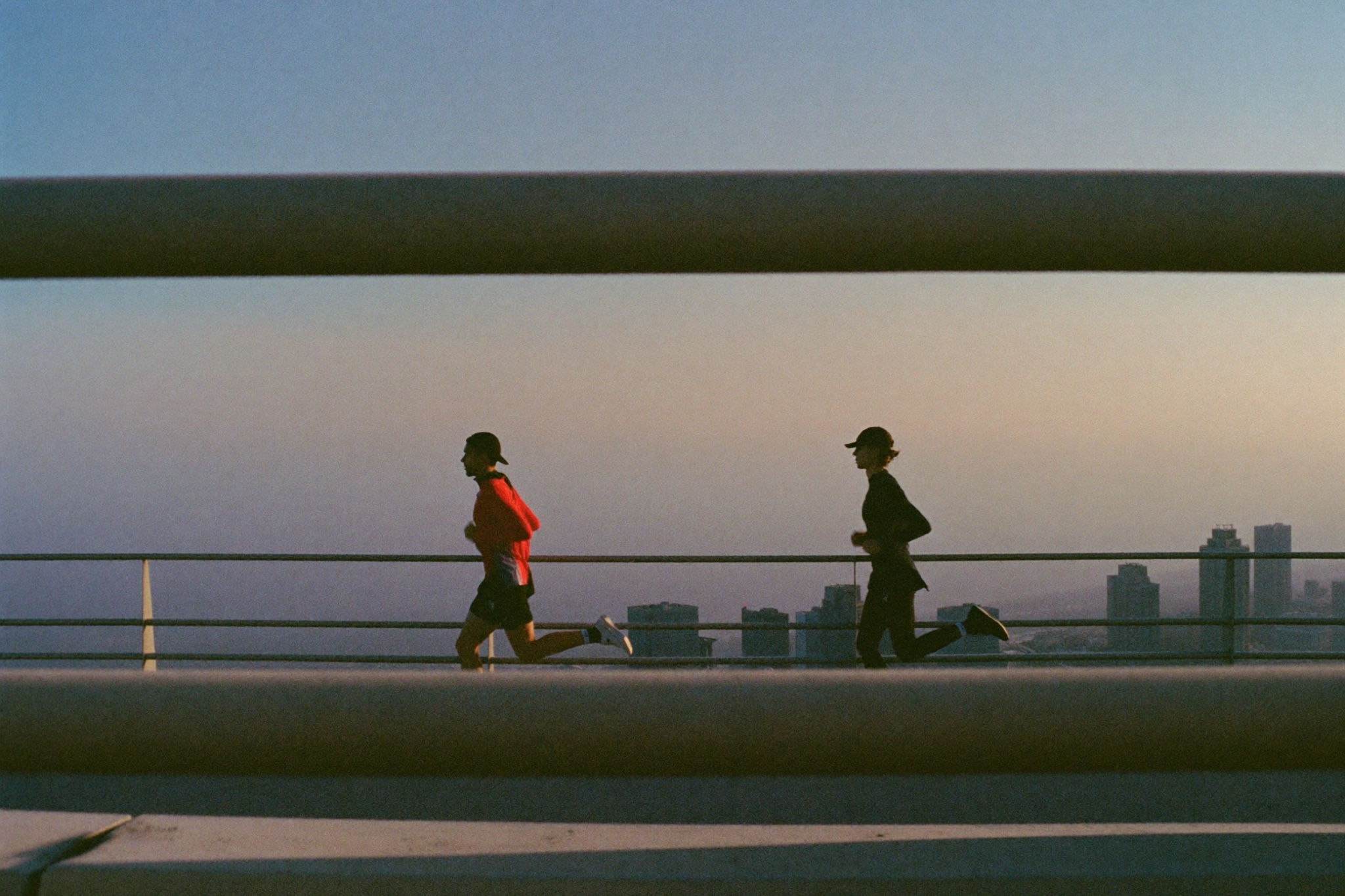 Two runners on an elevated overpass at blue hour